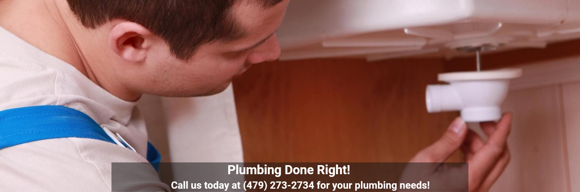 A plumber in blue overalls installing a white sink drain pipe. Overlay text reads: Plumbing Done Right! (479) 273-2734.