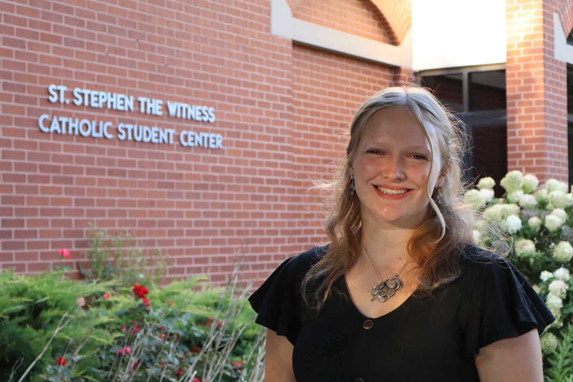 A young woman wearing a white sweater and a necklace smiles for the camera.