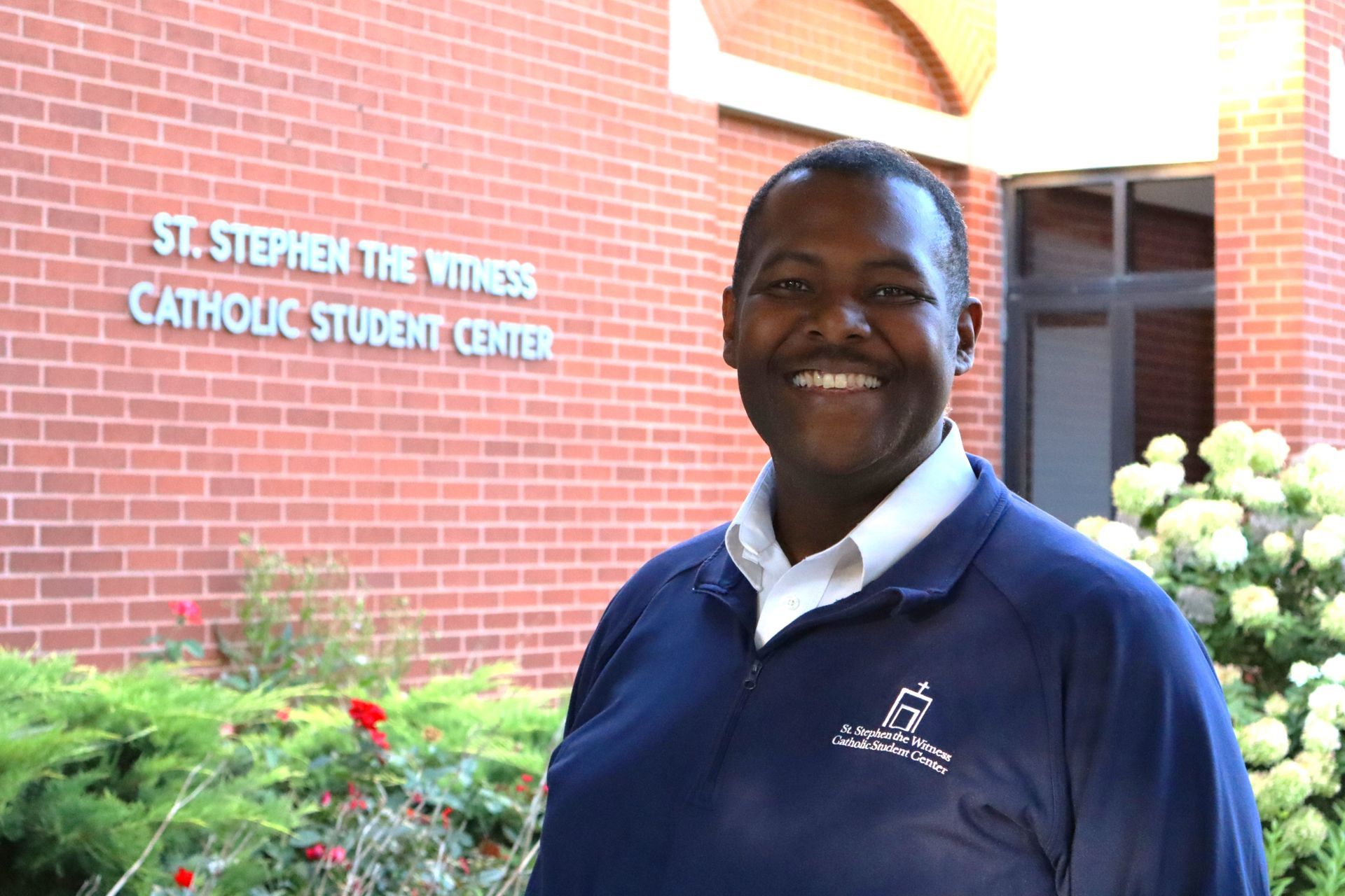 A man in a suit and tie is smiling in front of a brick wall.