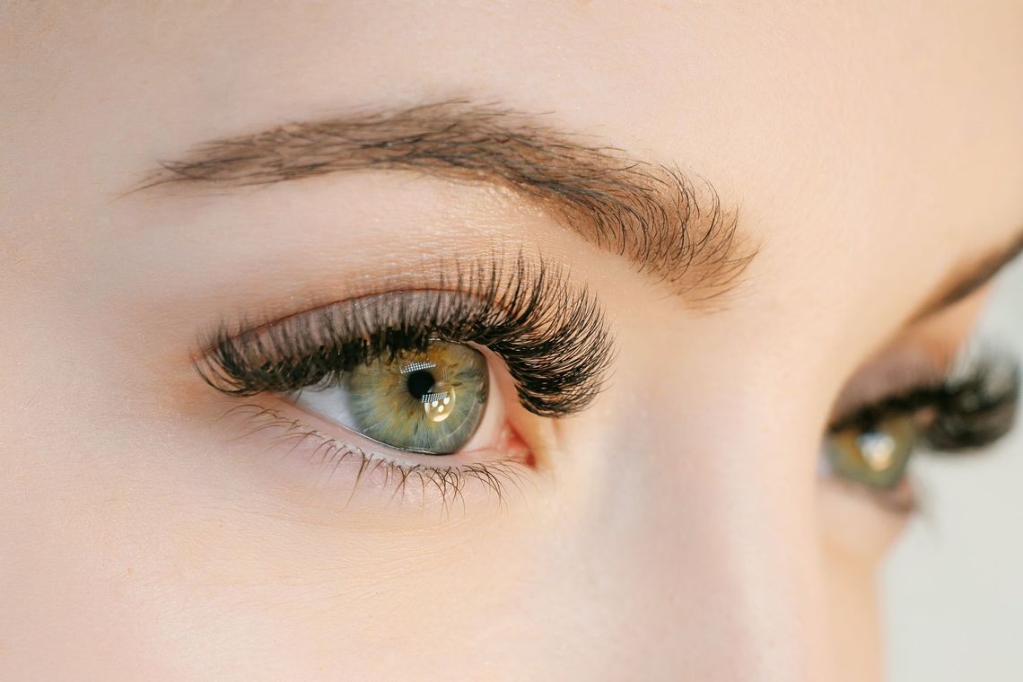 Close-up of a person's eye with long, dark eyelashes. Green iris, arched eyebrow.