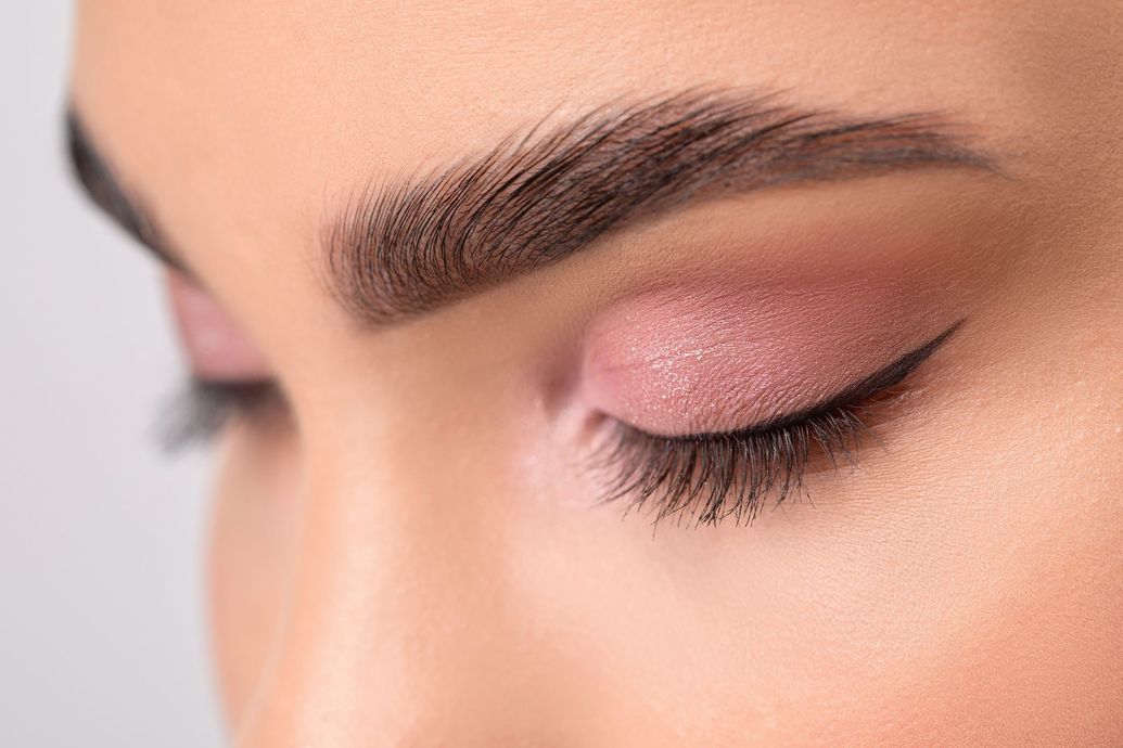 Close-up of a woman's eye with pink eyeshadow, black eyeliner, and thick eyebrows.