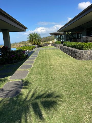 A grassy walkway lined with stone pavers connects two building wings under a bright blue sky with tropical landscaping.
