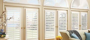 Three sets of white French doors with plantation shutters and matching arched fanlight windows in a bright room.