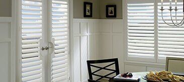 A bright room featuring white wainscoting, plantation shutters on French doors and windows, and a dining chair.