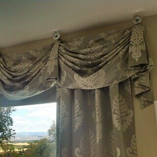 A beige damask-patterned fabric valance with elegant swag drapery hangs from circular ceiling-mounted fixtures.