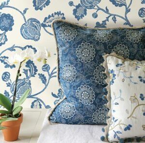 A blue and white floral-patterned wall serves as a backdrop for two decorative pillows and a potted white orchid.