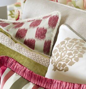 A close-up of decorative pillows in shades of green, red, and off-white featuring ikat, floral, and striped patterns.