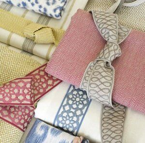 A variety of folded fabrics with patterns and textures in shades of red, blue, beige, and white, some tied with ribbons.