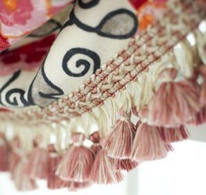 Close-up of a decorative lamp shade edge with cream-colored braiding and hanging dusty-pink tassels.