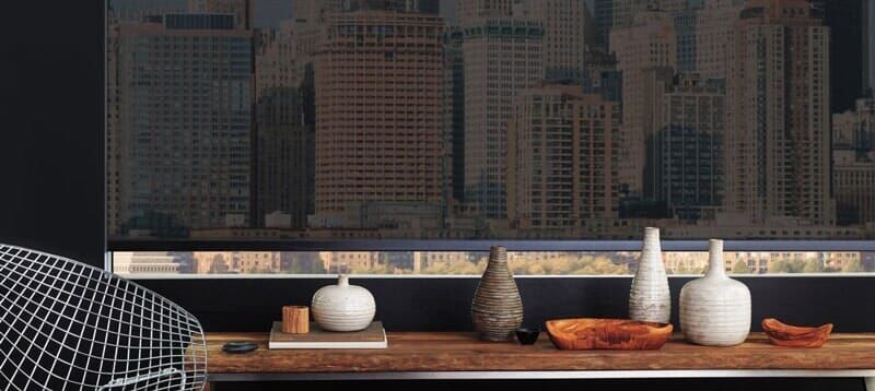 A wooden table holds four ceramic vases, a bowl, and a small object, positioned before a window with a city skyline view.