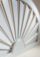 A decorative, arched wall mirror featuring a sunburst design with light-colored wooden rays against a mirrored background.