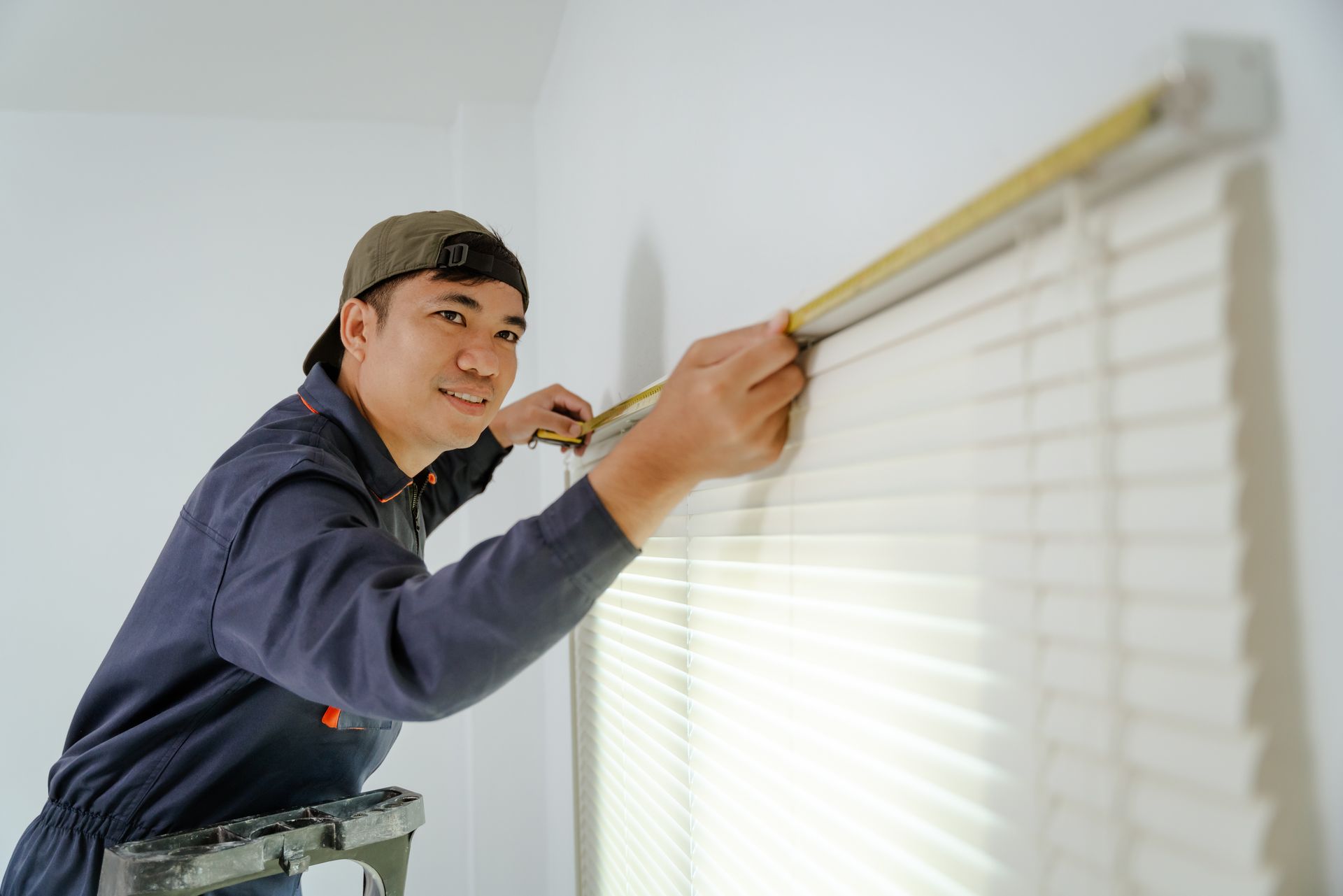 Professional installing custom blinds using measuring tape on window in residential space. Professional installing custom blinds using measuring tape on window in residential space.