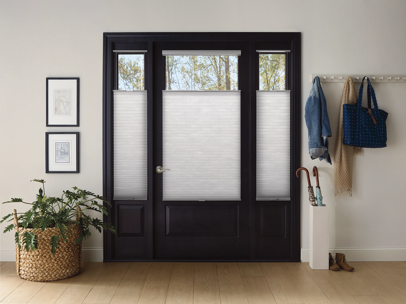 A dark-framed front door with sidelights featuring white top-down bottom-up cellular shades in a bright entryway.