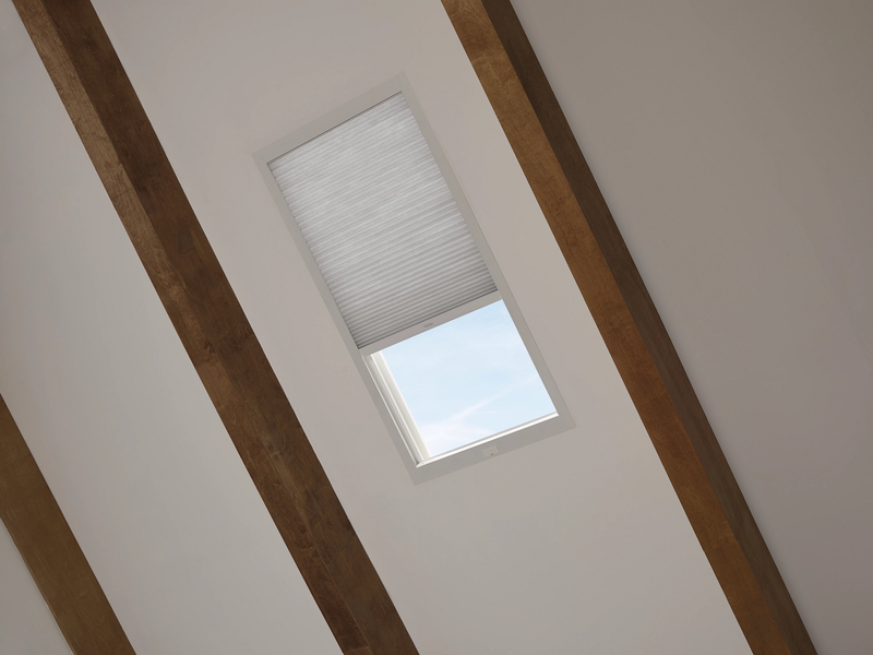 A white ceiling with two dark wood beams and a rectangular skylight featuring a partially closed pleated shade.