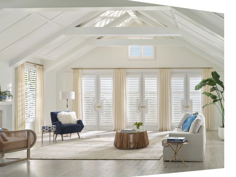 Bright, airy living room with a vaulted ceiling, white shutters on large windows, a navy chair, and a cream sofa.