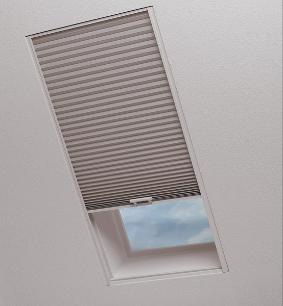 A beige pleated cellular shade partially covers a slanted skylight window, revealing a patch of blue sky and clouds below.