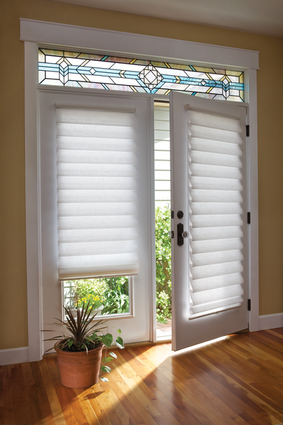 A pair of white French doors with pleated shades, a stained glass transom, and a potted plant on a wooden floor.