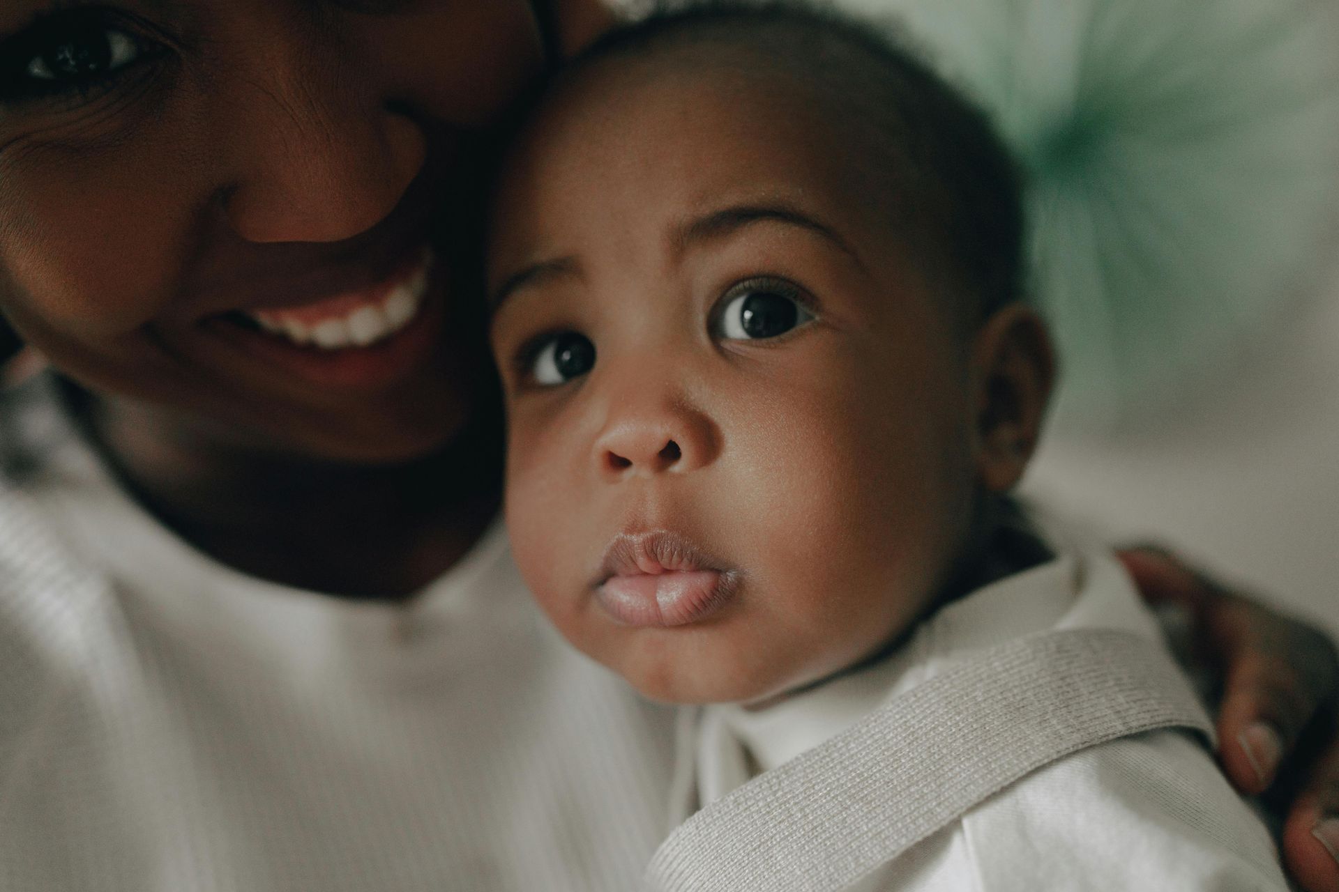 A close-up of a person holding a baby, who is looking directly at the camera with a neutral expression.