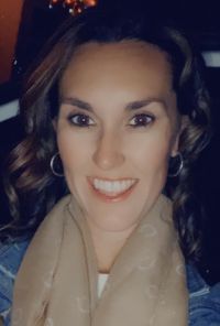 Woman with brown hair and smile, wearing hoop earrings and a scarf.