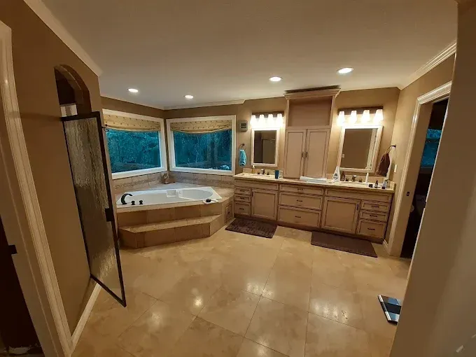 Spacious beige bathroom with a large tub by windows and a double vanity.