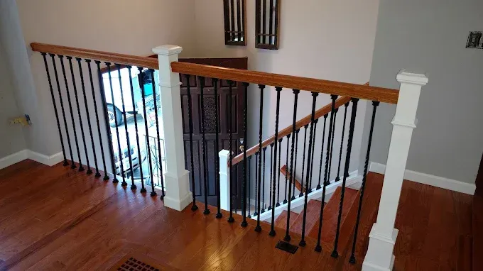 Wooden staircase with black spindles and light wood handrails, leading down.