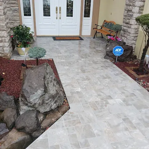 Pathway leading to a front door, with grey stone tiles. Includes a security sign and landscaping.