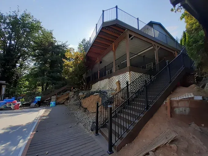 Two-story building with decks and stairs built into a hillside, stone foundation, black railing.