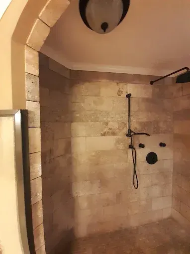 Shower with beige tile walls, black fixtures, and a curved entryway with stone tiles.