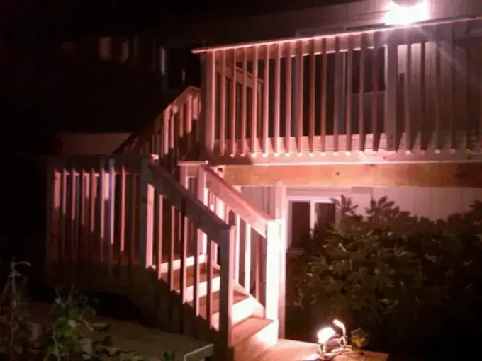 Wooden deck with stairs, illuminated at night. Railings and steps are visible.