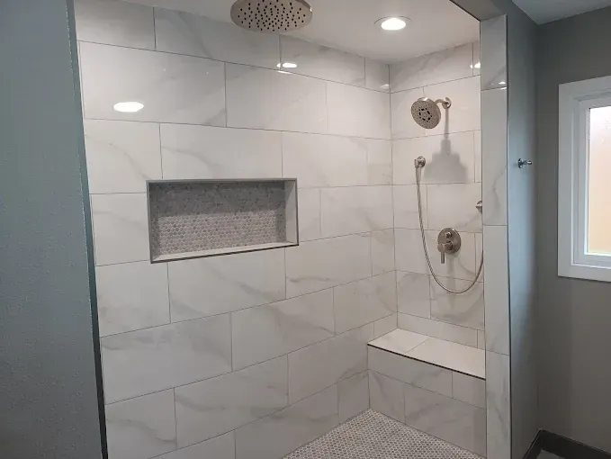 Tiled shower with a built-in bench and recessed shelf. Features rain showerhead, hand shower, and pebble floor.
