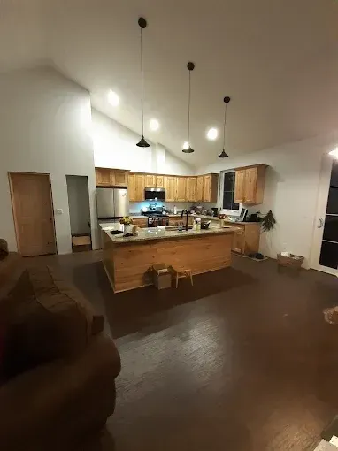 Kitchen with wooden cabinets, island, and dark wood floors, lit by pendant lights.