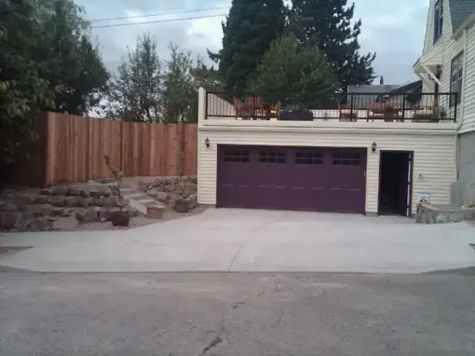 Garage with purple door, driveway, wooden fence, and rooftop deck on a cloudy day.