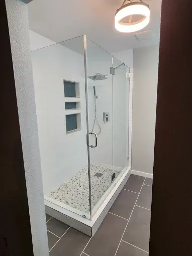 Modern shower with glass doors, white walls, stone floor, and gray tile floor.
