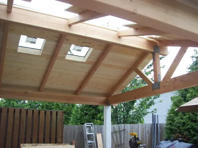 Wooden pergola roof with skylights, attached to posts; outdoor setting.