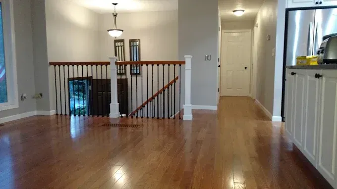 Spacious interior with hardwood floors, staircase with black spindles, neutral walls, and a hallway with a white door.