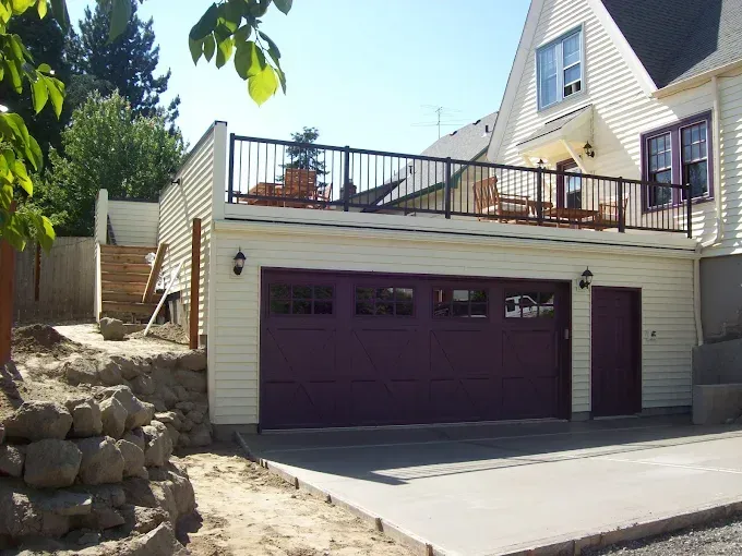 Two-story building: garage with purple door and deck with black railing.