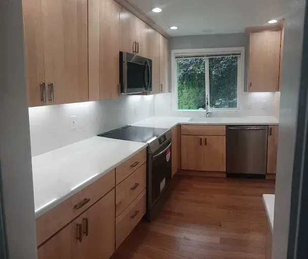Kitchen with light wood cabinets, white countertops, stainless steel appliances, and a window.