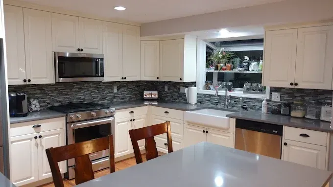 Cream-colored kitchen with stainless steel appliances, dark countertops, and a window above a white farmhouse sink.