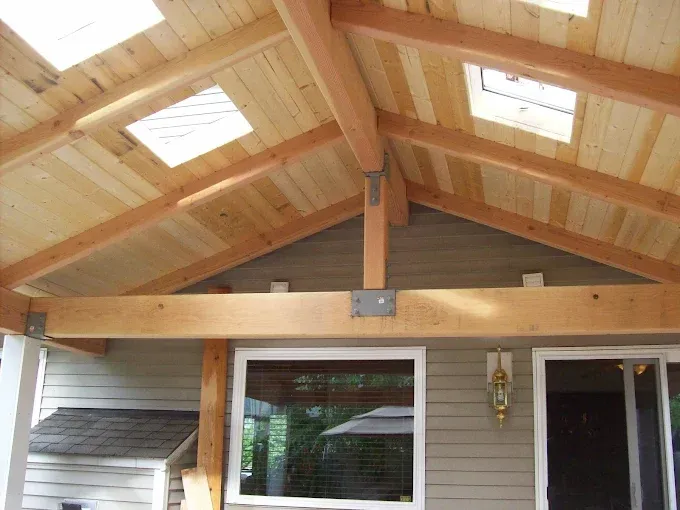 Wooden patio roof with skylights, beams, and support brackets.