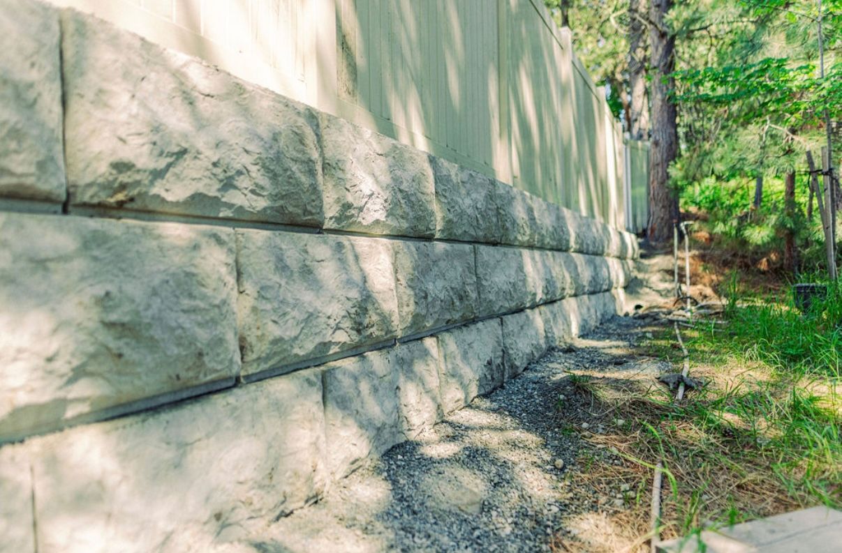 Stone block retaining wall, gray and tan, alongside grassy area and trees.