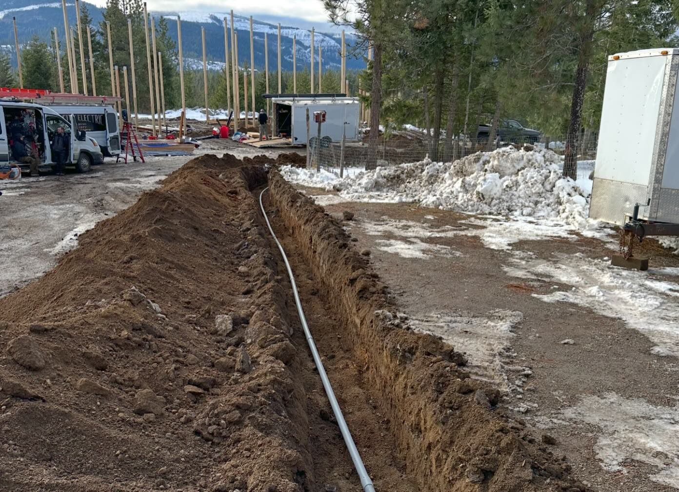 A trench with a white pipe running through it, likely for utilities, at a construction site in a snowy area.