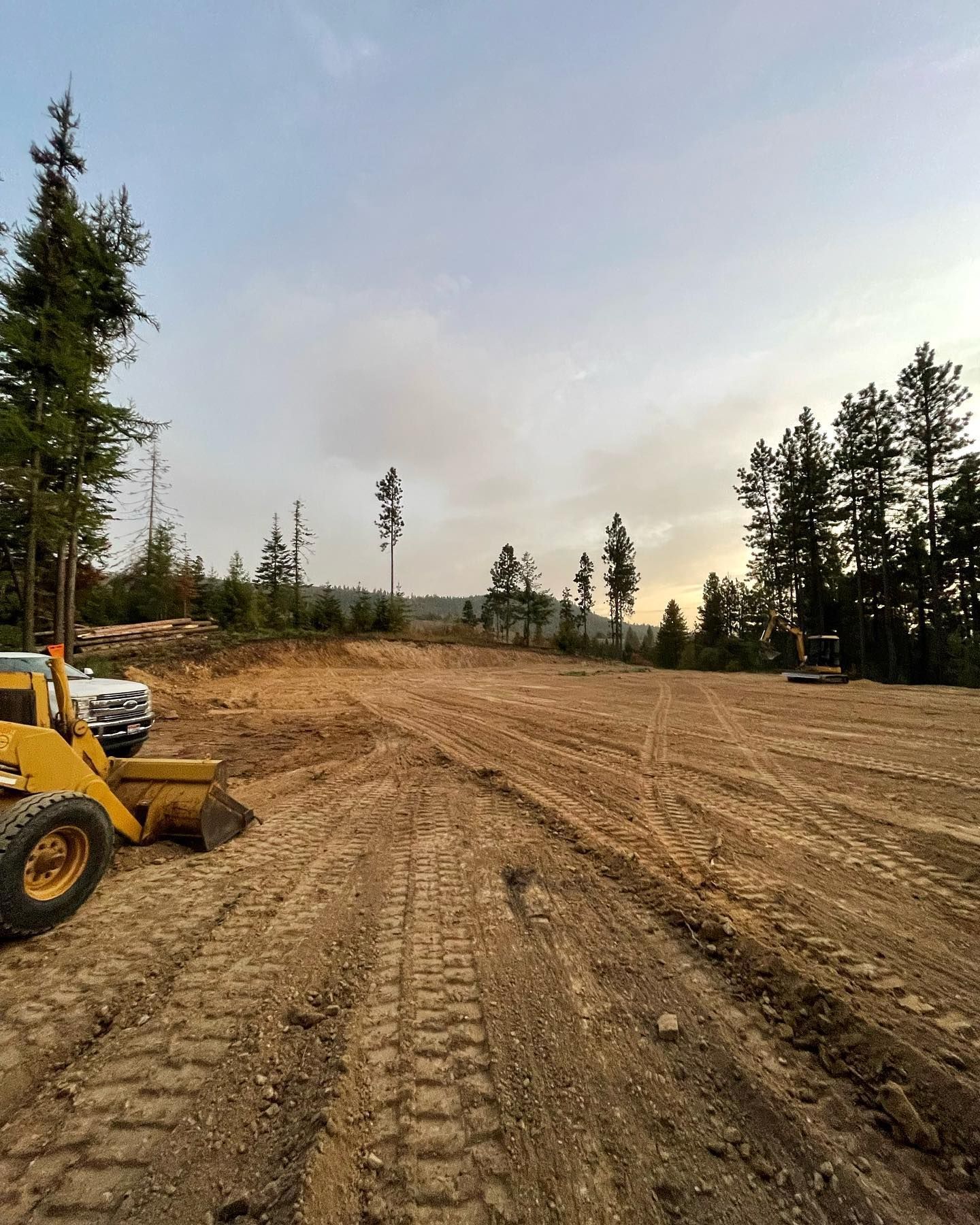 Cleared land with tractor, trees, and cloudy sky.