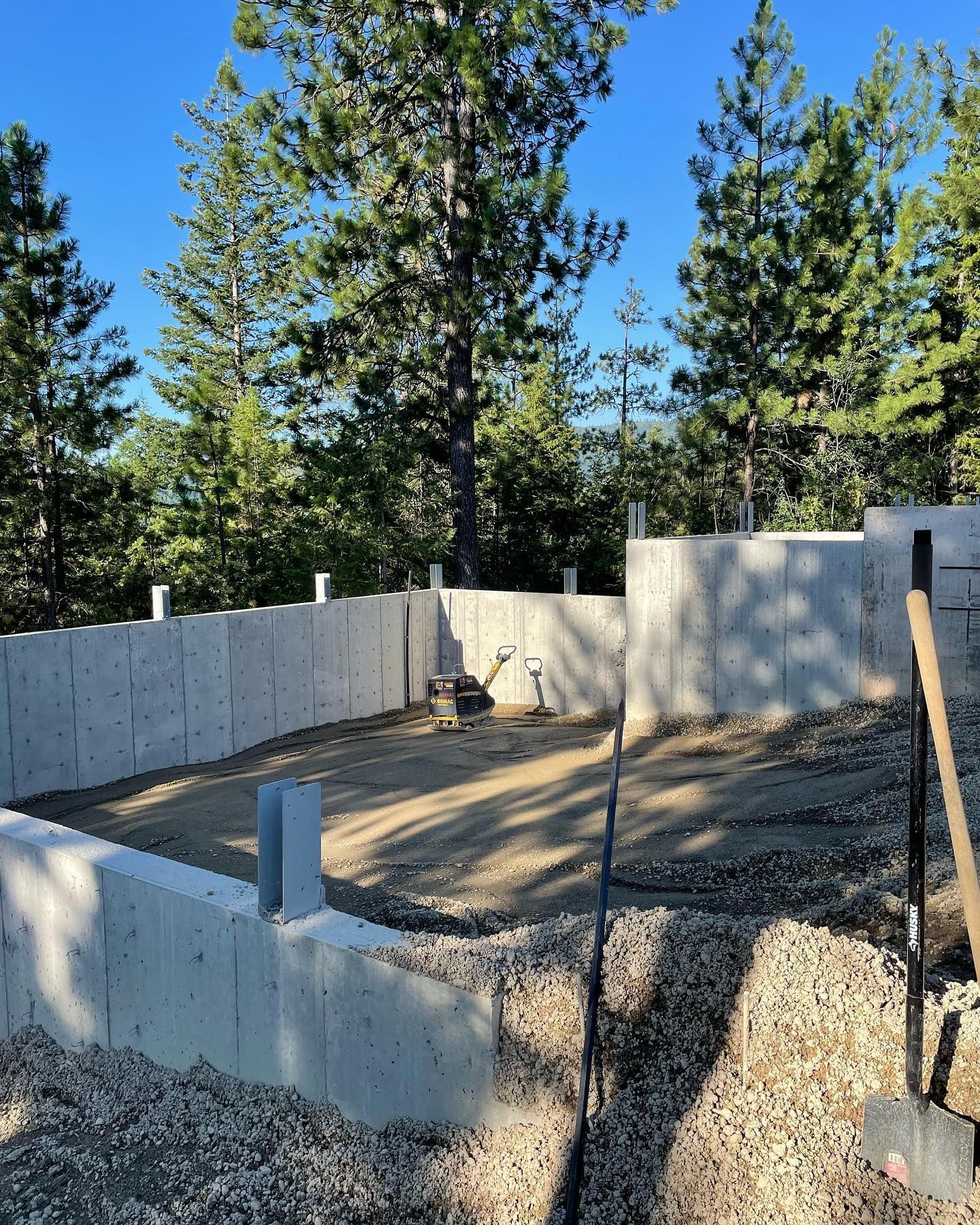 Concrete foundation of a building under construction, gravel base, surrounded by trees under a blue sky.