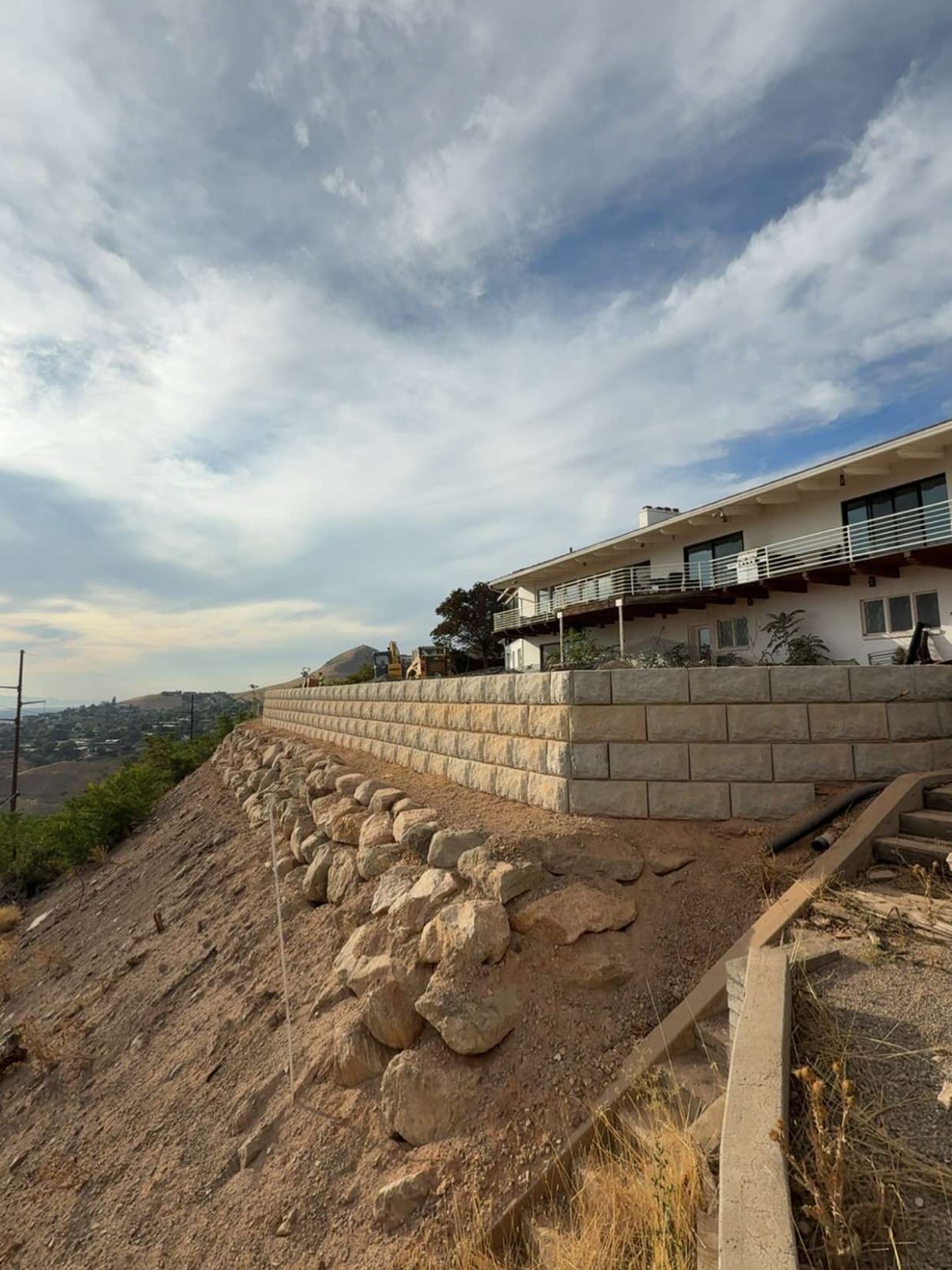 Retaining walls and house on hillside, against a cloudy sky.