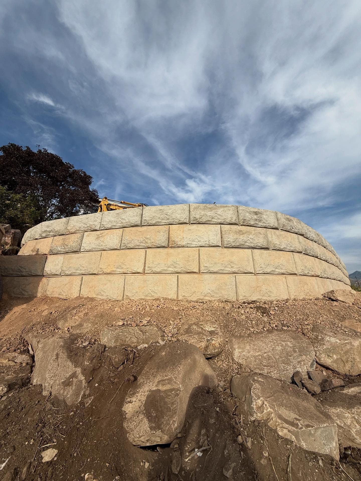 Retaining wall made of light-colored stone blocks, under a partly cloudy blue sky.