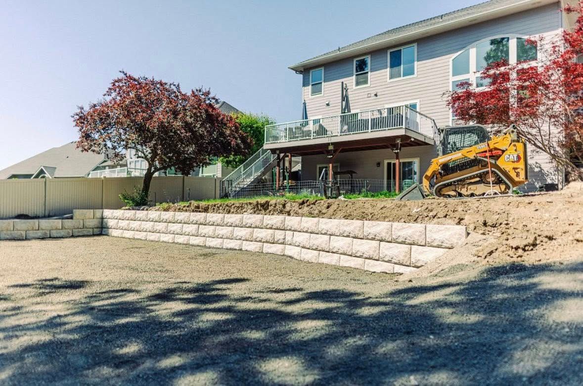 Backyard landscaping with retaining wall and bulldozer near a house.