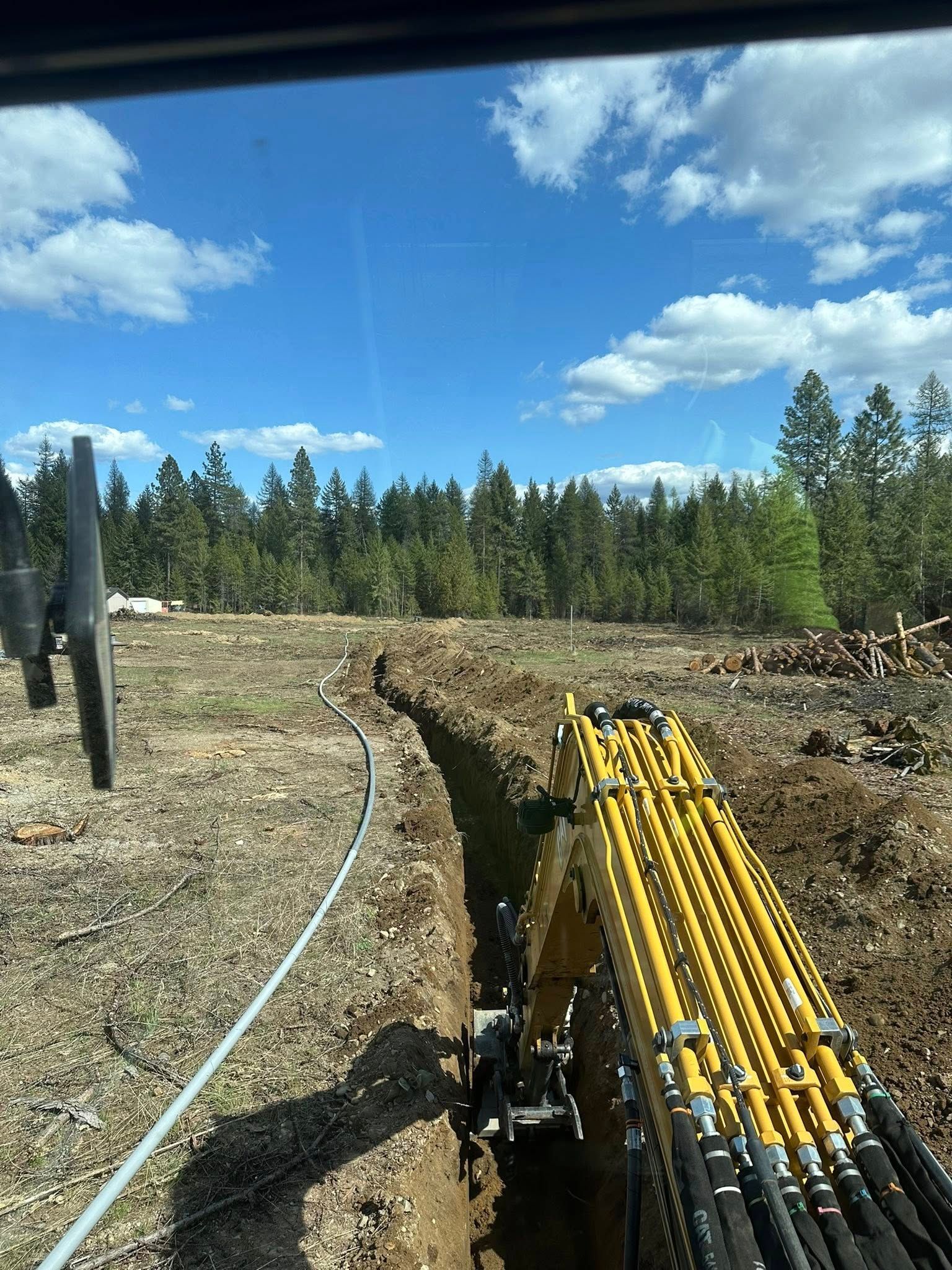 Yellow excavator digging a trench outdoors under a blue sky, with cable visible.