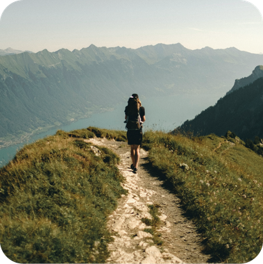 A person with a backpack is walking down a path in the mountains