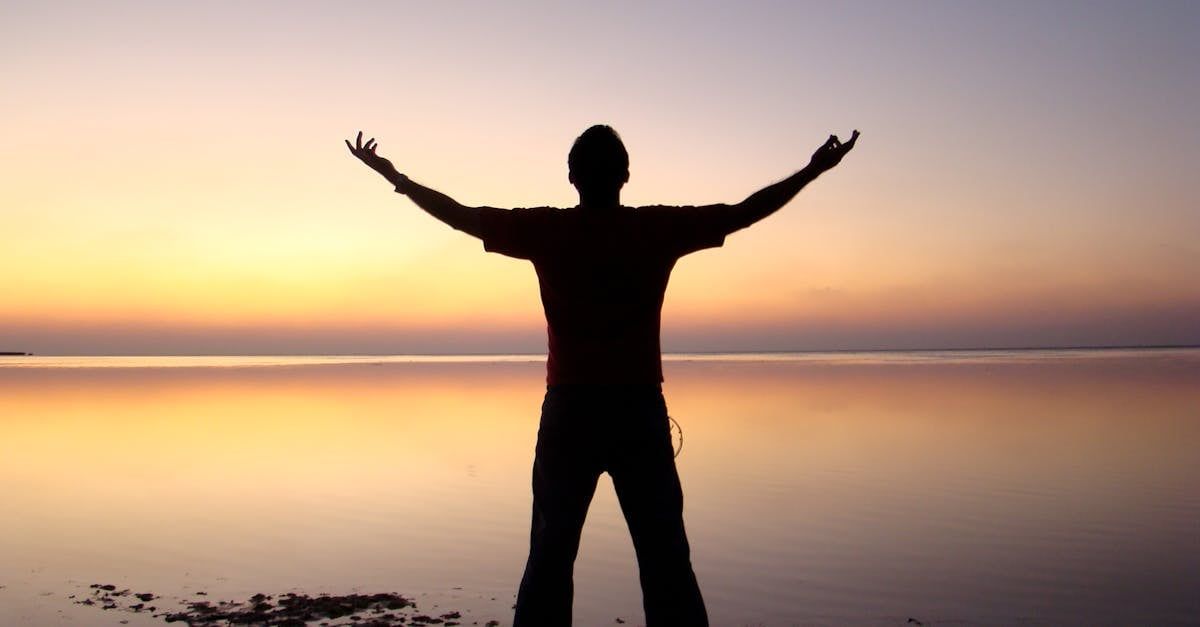 A silhouette of a man standing in front of a body of water with his arms outstretched