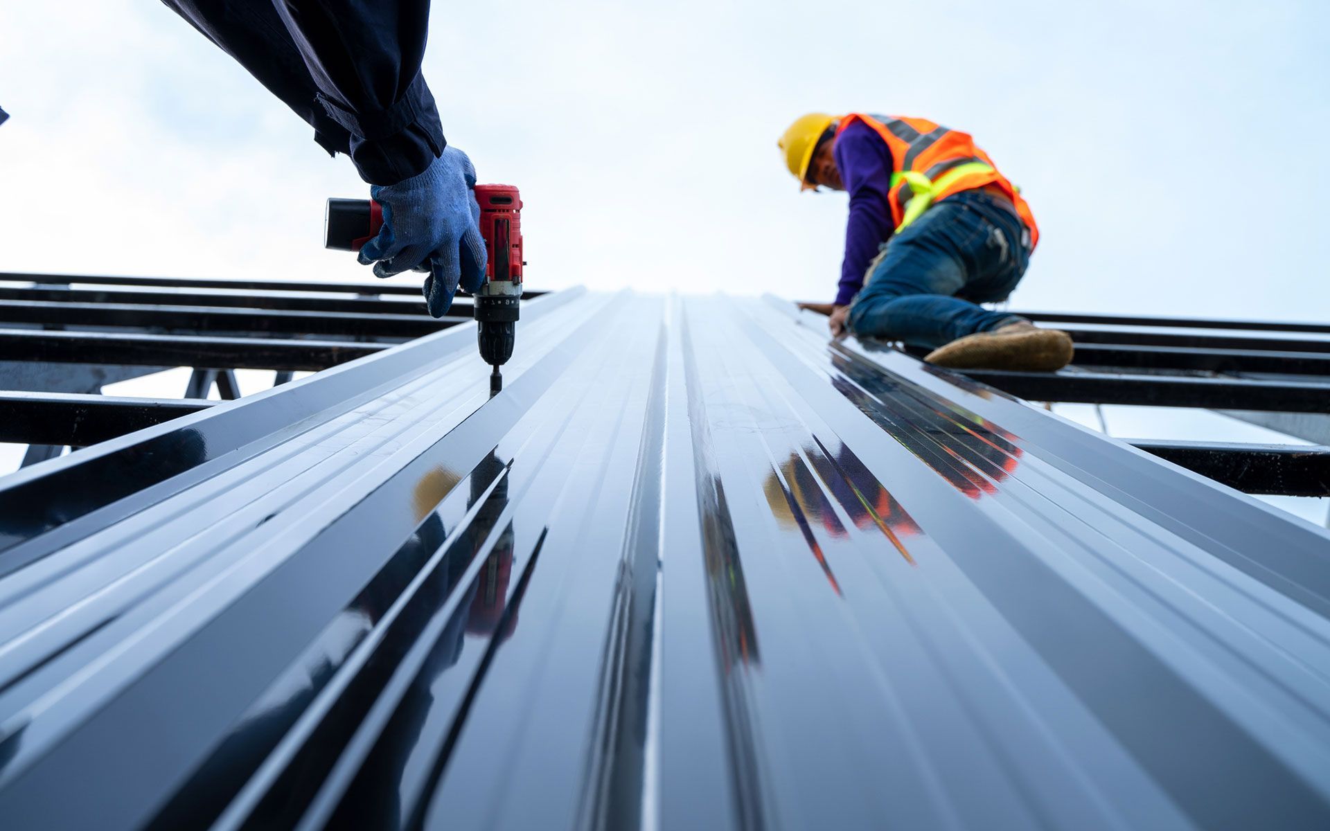 Two construction workers are working on a metal roof.
